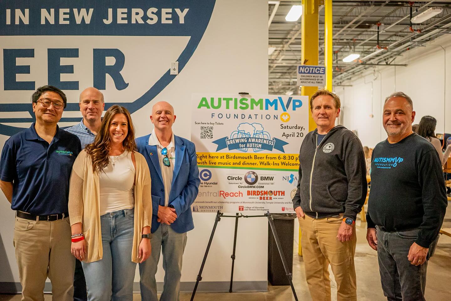 A group of five people standing in front of a sign, all smiling and happy.