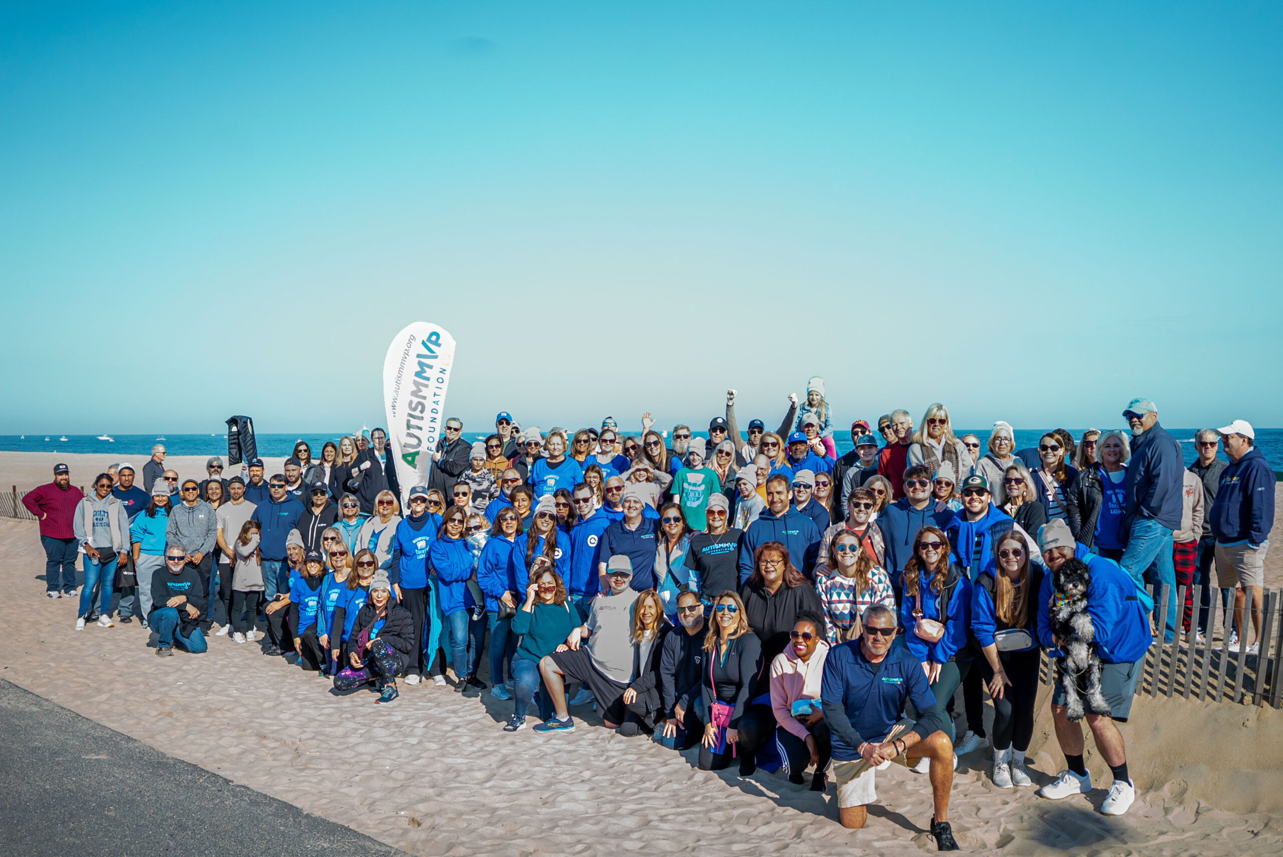 A group of people standing on a each on a clear, sunny day,